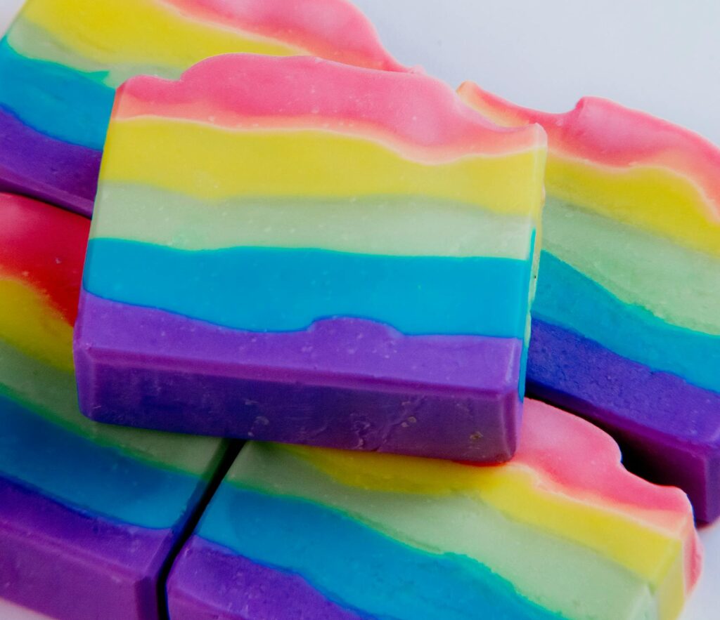 Colorful handmade rainbow soap bars stacked on a white background, perfect for body care product promotion.