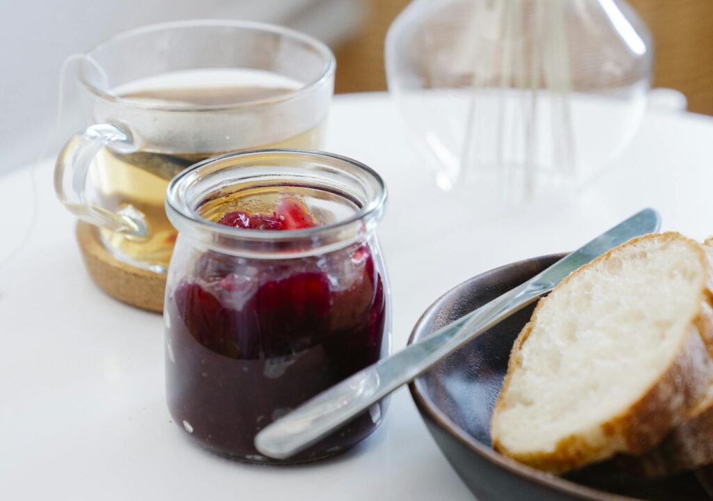 Warm breakfast setup with bread, jam, and tea on a white table indoors.