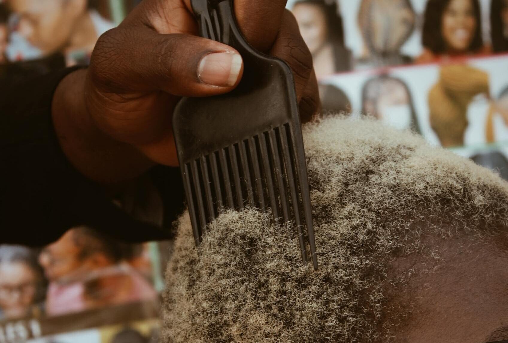 A person gets an Afro hairstyle styled with a pick comb at a salon, surrounded by hairstyle photos.